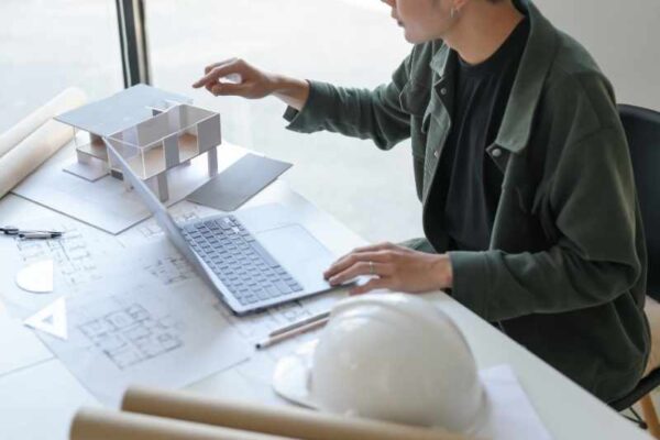 Fotografía de un plano arquitectónico extendido sobre una mesa de metal, con un casco de construcción y una tablet al lado. Luz de estudio, enfoque profesional.